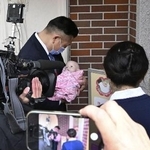 熊本市の慈恵病院を視察し、赤ちゃんポスト前で赤ちゃんの人形を抱く大阪府泉佐野市の千代松大耕市長（奥）＝２月