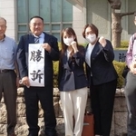 　判決後、代理人弁護士（両端）と共に「勝訴」と書いた紙を掲げる朝倉隆介さんら３人＝７月３０日、堺市