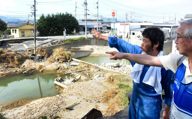 西日本豪雨で岡山県倉敷市真備町を流れる末政川の堤防の決壊場所について説明する男性（左）＝１１日午後４時６分、岡山県倉敷市真備町有井