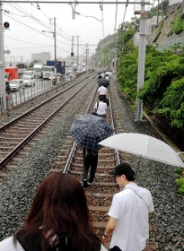山陽電鉄須磨浦公園－塩屋間で線路上に土砂が流れ込み、立ち往生した電車を降りて線路を歩く乗客ら＝６日午後３時２９分、神戸市垂水区塩屋町