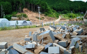 土砂崩れで山肌がむき出しになったままの共同墓地（中央奥）。掘り出された墓石の一部が路上に並ぶ＝丹波市氷上町横田