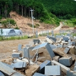 土砂崩れで山肌がむき出しになったままの共同墓地（中央奥）。掘り出された墓石の一部が路上に並ぶ＝丹波市氷上町横田