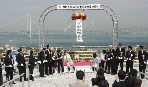 明石海峡大橋を背景に、くす玉を割って開通１０年を祝う式典出席者＝５日午前、淡路市岩屋の神戸淡路鳴門自動車道・淡路サービスエリア（撮影・峰大二郎） 