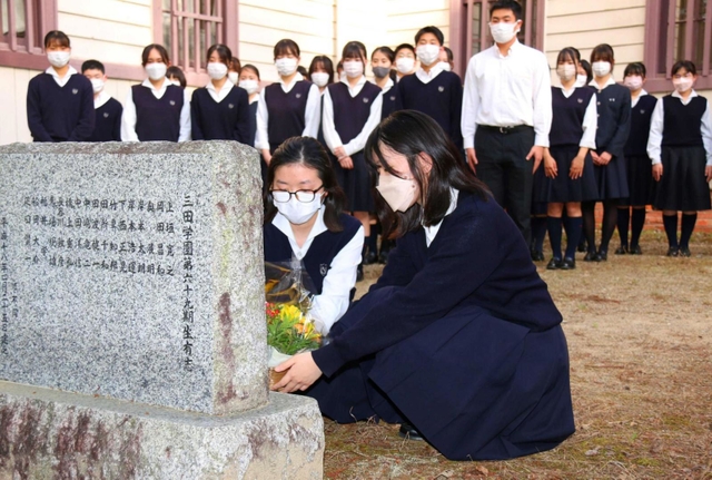 石井勝さんの顕彰碑に花を手向ける吹奏楽部の生徒＝三田学園