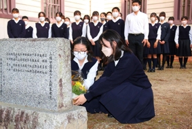 石井勝さんの顕彰碑に花を手向ける吹奏楽部の生徒＝三田学園