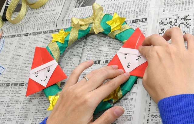 （２）折り紙サンタ、モールやシール、好きな形に切った色画用紙で（１）を飾り付ける。つり下げる部分にリボンを付けて出来上がり