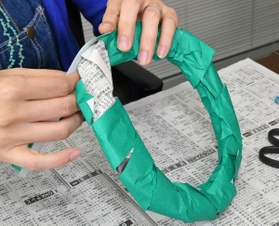 （１）新聞紙を細長く丸め、両端をセロハンテープでとめて輪にする。緑や黄緑の折り紙を短冊状に切り、輪に巻き付けながら貼る
