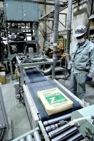 袋詰めされた耐硫酸性モルタルを確認する従業員。品質維持のため、大型ミキサーも独自の改良を加えているという＝明石市硯町３