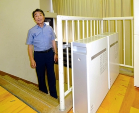 太陽光発電の電気をためる蓄電池と西山俊介さん＝朝来市山東町溝黒