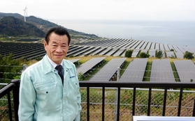太陽光発電所や隣にある風力発電所について説明する松村孝一さん＝淡路市野島貴船