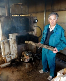 多い日には１５０本の廃原木を燃料に使う暖房施設と中西郁さん＝三田市上相野