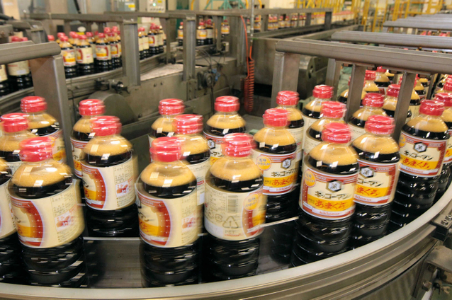 ベルトコンベヤーで箱詰めの作業工程に向かうしょうゆのボトル 