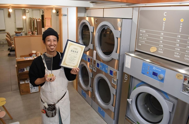 「コインランドリーアワード」最優秀賞を受賞した「ハル」の浜田健太さん。コインランドリーの奥に美容室が見える＝高砂市米田町古新
