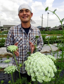 種採り用に残したニンジンの株から咲く白い花と神崎一馬さん＝姫路市香寺町行重