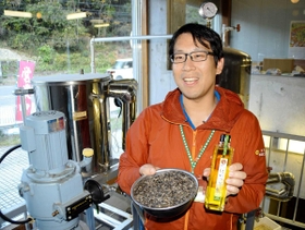 搾油設備の前で、ひまわり油と原料の種を持つ平福祐介館長＝兵庫県佐用町船越、南光ひまわり館
