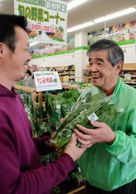 生産者の山里剛史さん（左）からホウレンソウを受け取る井上正和さん＝神戸市垂水区小束台、めぐみの郷学園南店