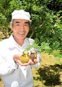 爽やかな香りが広がる自身の畑で定番のつくだ煮（右）と「山椒ジェノベーゼ」を持つ梅谷幸男さん＝養父市畑