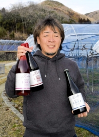 ブドウ畑を前に、できたばかりの３種のワインを手にする田中源道さん＝兵庫県上郡町細野