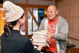 コメを９合ずつ小分けした袋を女性店員に手渡す「いづよね」の川崎恭雄代表取締役（右）。パーカーの下のＴシャツがユニホームだ＝神戸市東灘区本山北町３、いしころカフェ（撮影・風斗雅博）