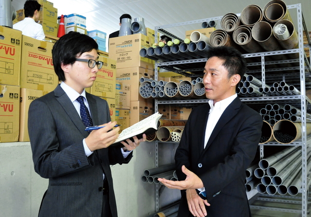 倉庫にある約3千種類の資材について解説する松田幸治社長（右）