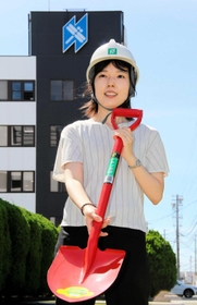 創業製品のシャベルを持つ日工の岡橋早苗さん。本社棟にはトンボ印が描かれている。撮影した中庭にはトンボが舞っていた＝明石市大久保町江井島