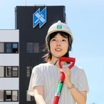 創業製品のシャベルを持つ日工の岡橋早苗さん。本社棟にはトンボ印が描かれている。撮影した中庭にはトンボが舞っていた＝明石市大久保町江井島