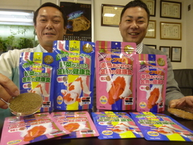 発売から３０年を超した金魚の餌を手にする山本直之さん（左）と村上恵介さん。観賞魚用飼料は海外４０カ国以上に輸出されている＝姫路市南町９
