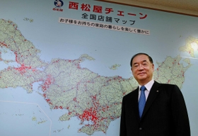 店舗がある場所に赤いシールを貼った全国地図の前で笑顔を見せる大村禎史社長＝姫路市飾東町庄