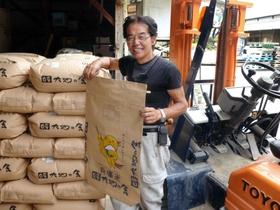 袋詰めされた新米の前に立つ衣笠愛之さん。袋にあしらった人気マスコット「はばタン」で兵庫県産をアピールする＝姫路市夢前町宮置