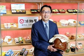 駅弁の見本が並ぶ淡路屋本社のショーケース前で、人気商品「ひっぱりだこ飯」の２０倍サイズの器を手に戦略を語る寺本督社長＝神戸市東灘区魚崎南町３