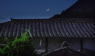 如意輪寺の石段下に椎名麟三が９～１５歳まで過ごした旧居が今もたたずむ。夕暮れ時、屋根瓦の向こうに月が浮かんだ＝姫路市書写（撮影・三津山朋彦）