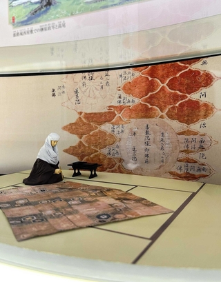 姫路文学館の榊原政岑・高尾太夫のコーナー。打敷に政岑の法名をしたためる高尾を人形で再現し、その筆跡を背景に配している＝姫路市山野井町