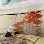 姫路文学館の榊原政岑・高尾太夫のコーナー。打敷に政岑の法名をしたためる高尾を人形で再現し、その筆跡を背景に配している＝姫路市山野井町