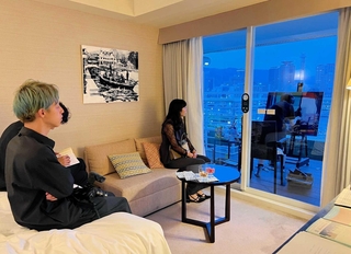 ホテル客室のバルコニーで制作する久保田沙耶さん（右、後ろ姿）とその様子を見つめる参加者たち＝神戸市中央区波止場町