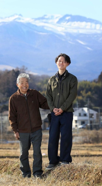 まちのシンボル安達太良山をバックに立つ長男の塚田晴さん（右）。憧れの有機農家大内信一さん（左）は原発事故を乗り越え、顧客を取り戻してきた。晴さんを頼もしげに見つめる大内さんは「あと１０年長生きして成長を見届けたい」＝福島県二本松市