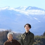 まちのシンボル安達太良山をバックに立つ長男の塚田晴さん（右）。憧れの有機農家大内信一さん（左）は原発事故を乗り越え、顧客を取り戻してきた。晴さんを頼もしげに見つめる大内さんは「あと１０年長生きして成長を見届けたい」＝福島県二本松市