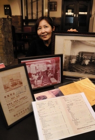 創業当時のメニュー表や、祖父を収めた写真を手にする鈴木真紀子さん。「歴史の重みを感じます」＝御影公会堂