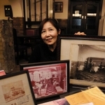 創業当時のメニュー表や、祖父を収めた写真を手にする鈴木真紀子さん。「歴史の重みを感じます」＝御影公会堂