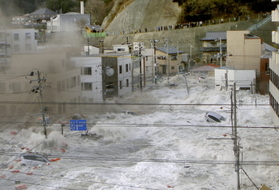 岩手県釜石市の市街地を襲う津波。後方の高台には多くの避難者の姿が見える＝２０１１年３月、海上保安庁提供