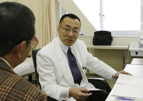 診療室で医師の冨田尚裕さん（右）の前に座って治療の説明を受ける。「不安もあるが、期待の方が大きい」と２度目の手術を心待ちにする＝西宮市武庫川町、兵庫医科大学病院（撮影・長嶺麻子）