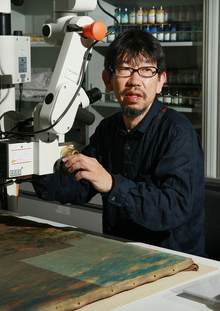 大型顕微鏡の前に座る田中千秋さん。「作品より絵の状態が気になってしまうので、ほかの美術館には行けなくなった」と苦笑する＝神戸市中央区脇浜海岸通１、兵庫県立美術館（撮影・神子素慎一） 