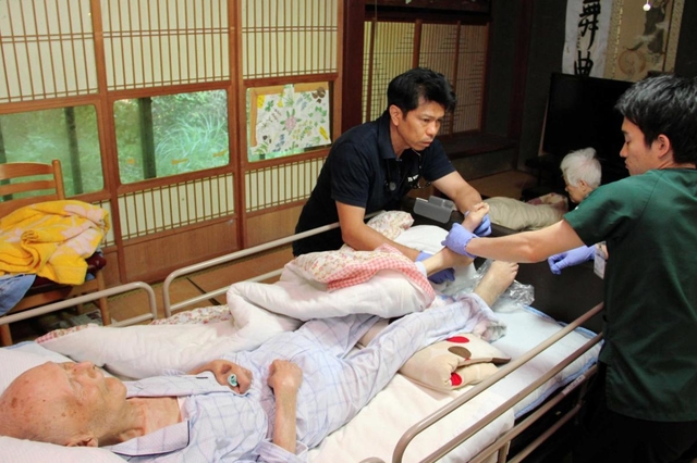 上田満さん、昌子さん夫妻の自宅を訪れ診療する花戸貴司医師（左）＝滋賀県東近江市