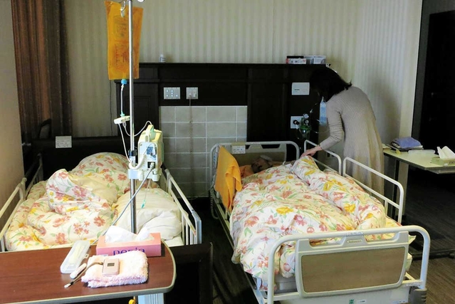 ベッドを並べて過ごす金森英彦さん（右）と克子さん。２人を支える長女の宮本亜紀子さん＝芦屋市立芦屋病院