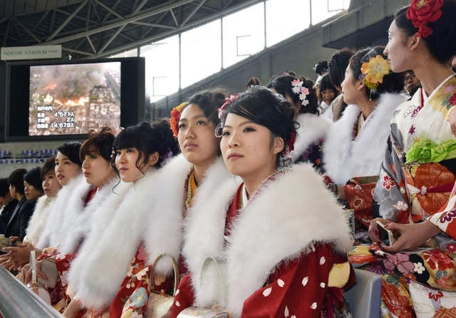 大型スクリーンに映し出される阪神・淡路大震災当時の街の様子を見つめる新成人＝１１日午後、神戸市兵庫区御崎町１、ノエビアスタジアム神戸（撮影・風斗雅博）