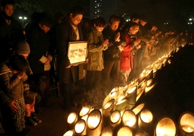 震災２１年を迎え、竹灯籠を前に黙とうする人たち＝１７日午前５時４６分、東遊園地（撮影・大森　武）