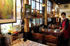 お気に入りの絵画やランプシェードを飾った店内と店主の永井芳子さん＝尼崎市東難波町５