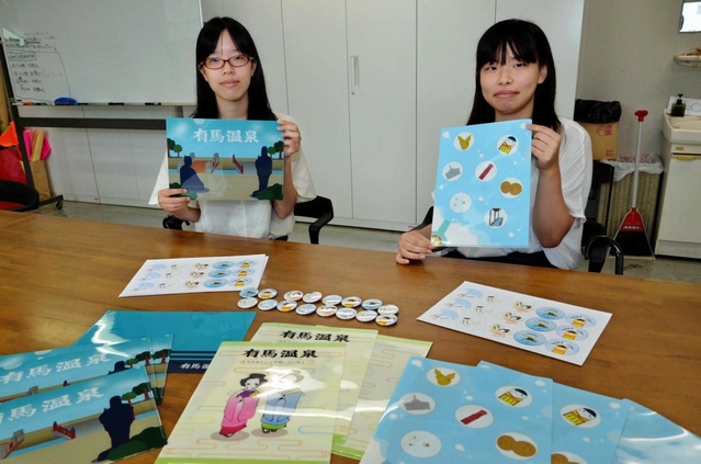 自作した缶バッジとクリアファイルを紹介する学生たち＝神戸芸術工科大学