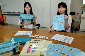 自作した缶バッジとクリアファイルを紹介する学生たち＝神戸芸術工科大学