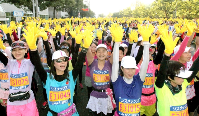 阪神・淡路大震災からの復興の象徴「ひまわり」をイメージした黄色い手袋がスタート前に配られ、２万人のランナーが両手を掲げて「感謝と友情」を表現した＝２３日、神戸市中央区磯辺通４（撮影・峰大二郎）