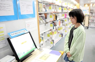 予約していた本を借りる新開彩永さん。本は奥の棚に届いていて、機械で確認することができる＝神戸市東灘区住吉東町２